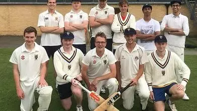 The Trinity College Cricket team crouched in front of a clubhouse