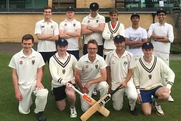 The Trinity College Cricket team crouched in front of a clubhouse